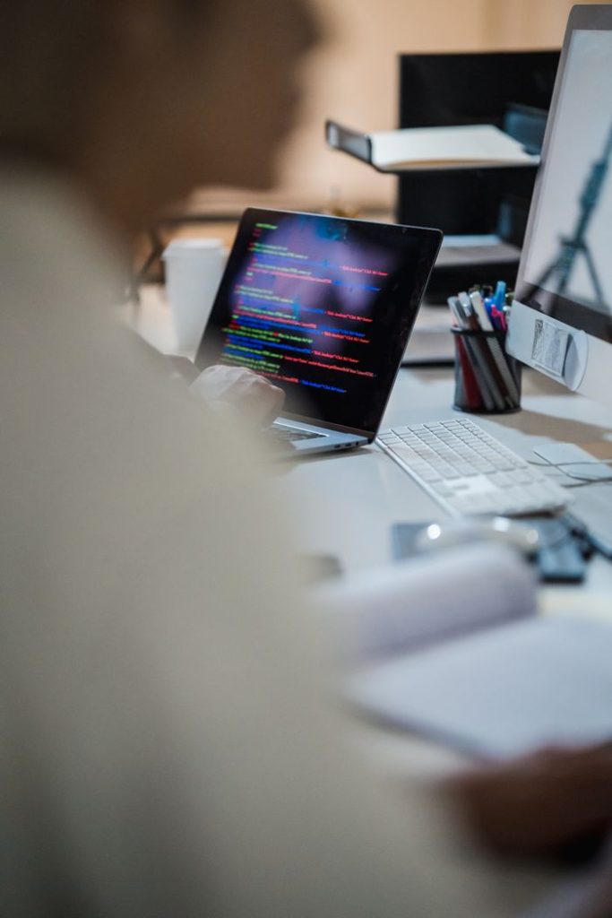 The Art of Drawing Readers In: Your attractive post title goes here Blurred figure at a desk with a laptop displaying colorful code, indicating a programming environment.